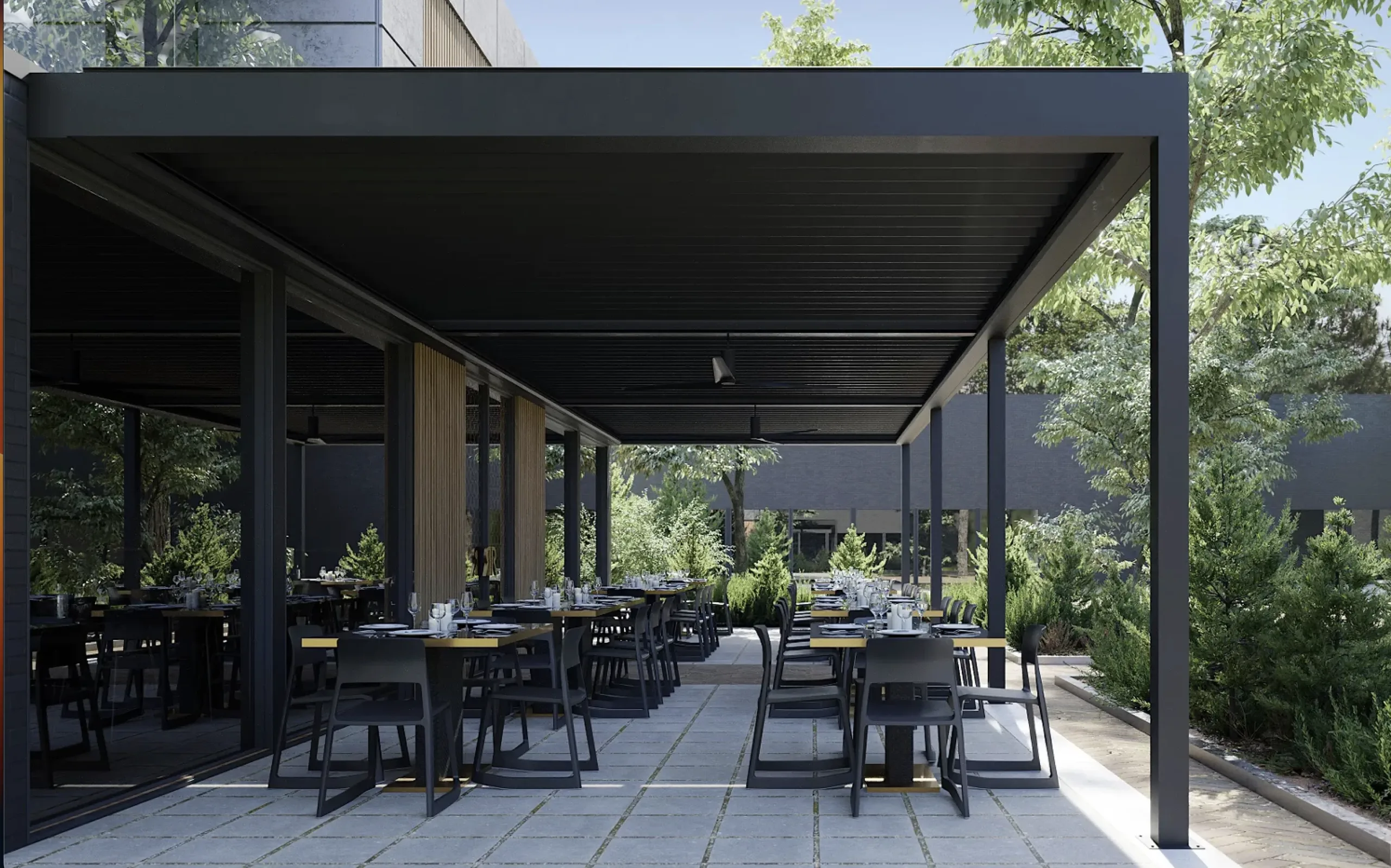 A spacious commercial alfresco dining area with modern black furniture on a light gray stone tile floor, surrounded by lush green trees and landscaping.