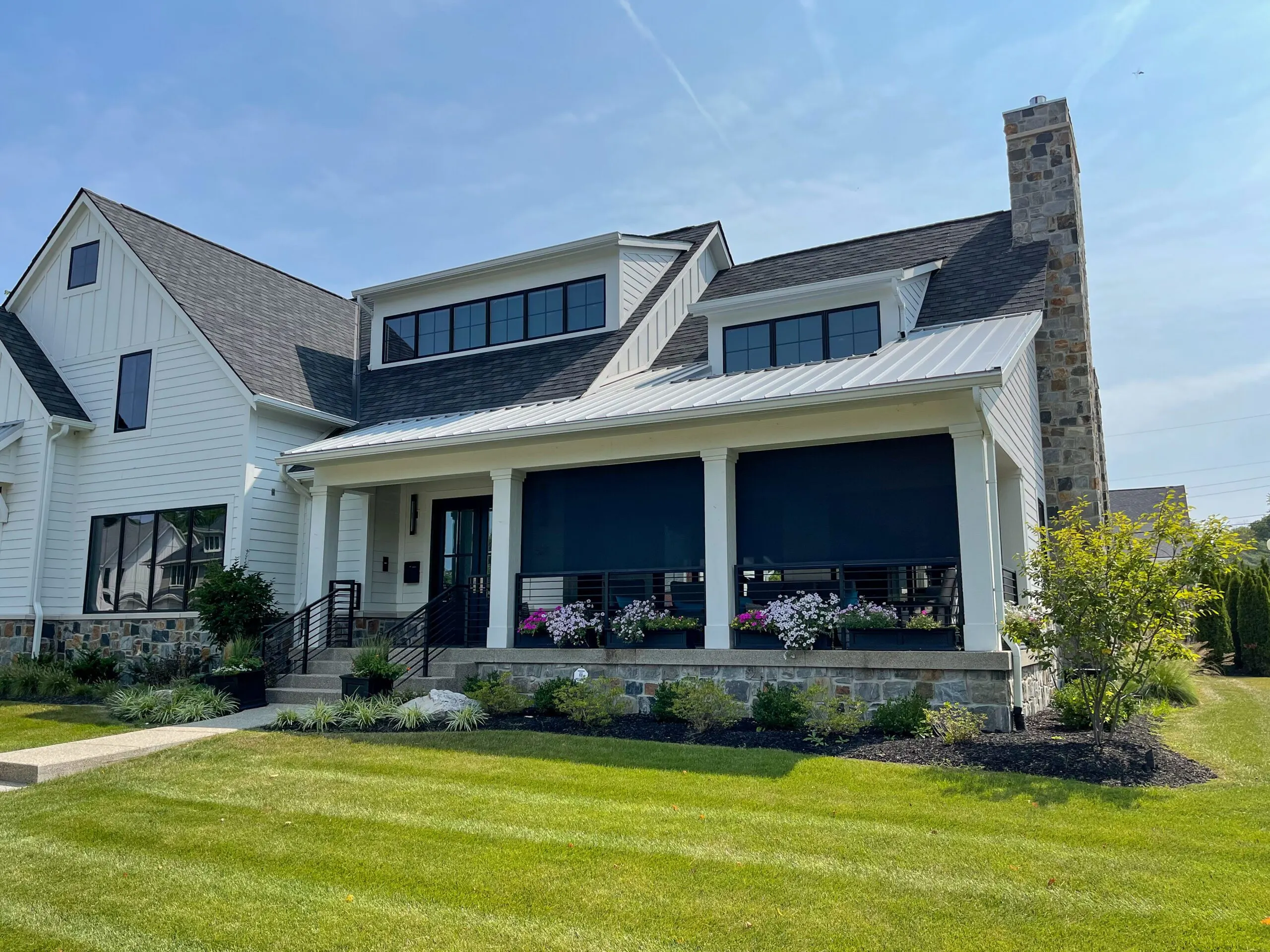 Modern farmhouse exterior design showcasing motorized retractable porch screens, white vertical siding, and a stacked stone foundation wall.