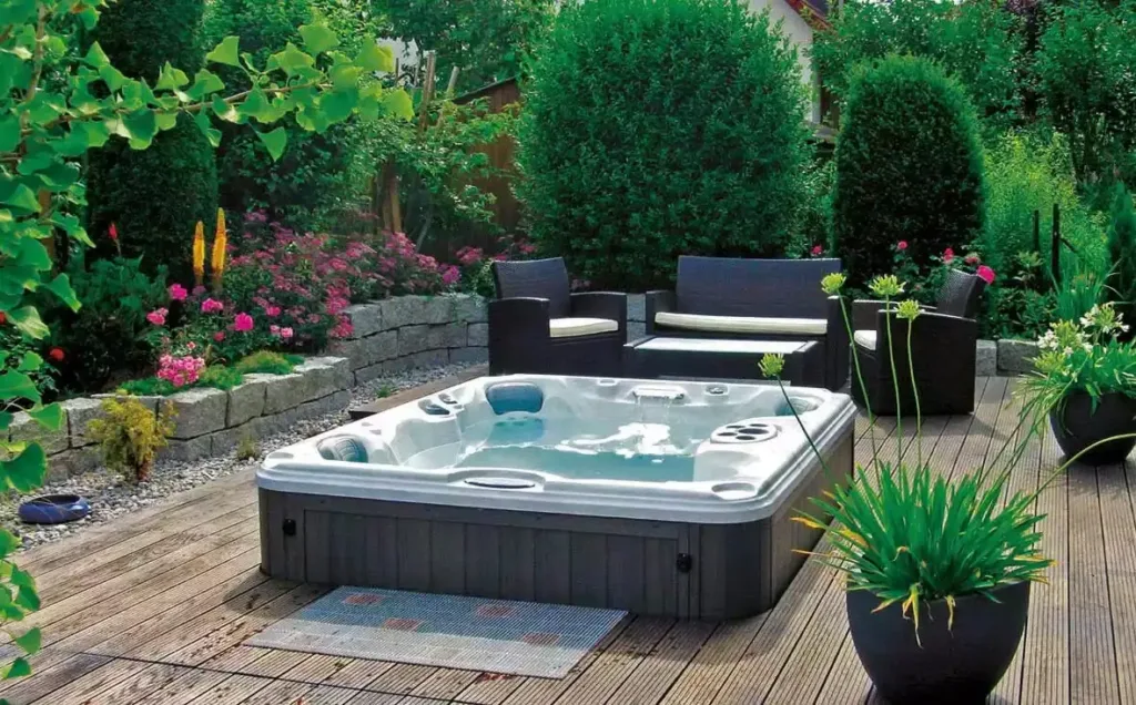Outdoor hot tub on wooden deck surrounded by lush garden and patio seating area