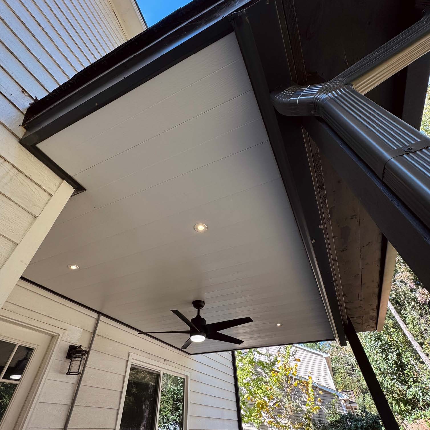 Custom white under-deck ceiling system with a black outdoor fan for water drainage and outdoor living dry space expansion.