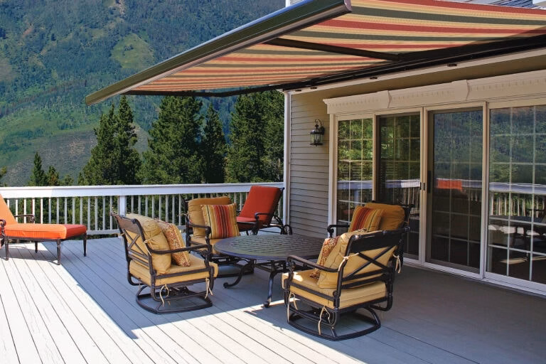Custom retractable patio deck awning installation providing UV shade protection for outdoor furniture with a beautiful mountain landscape view.