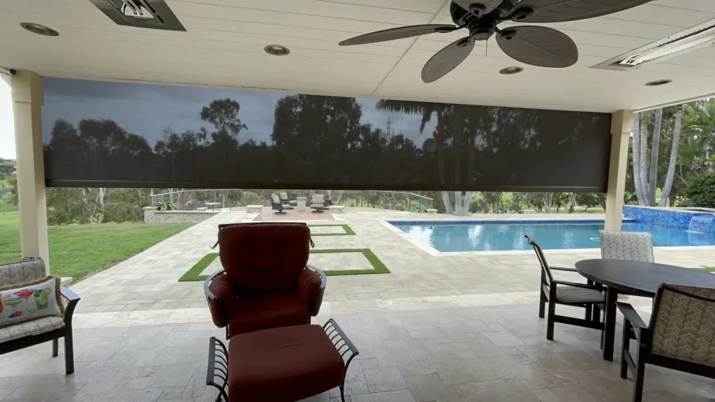 Covered patio with motorized retractable screen partially lowered, overlooking a pool and landscaped backyard