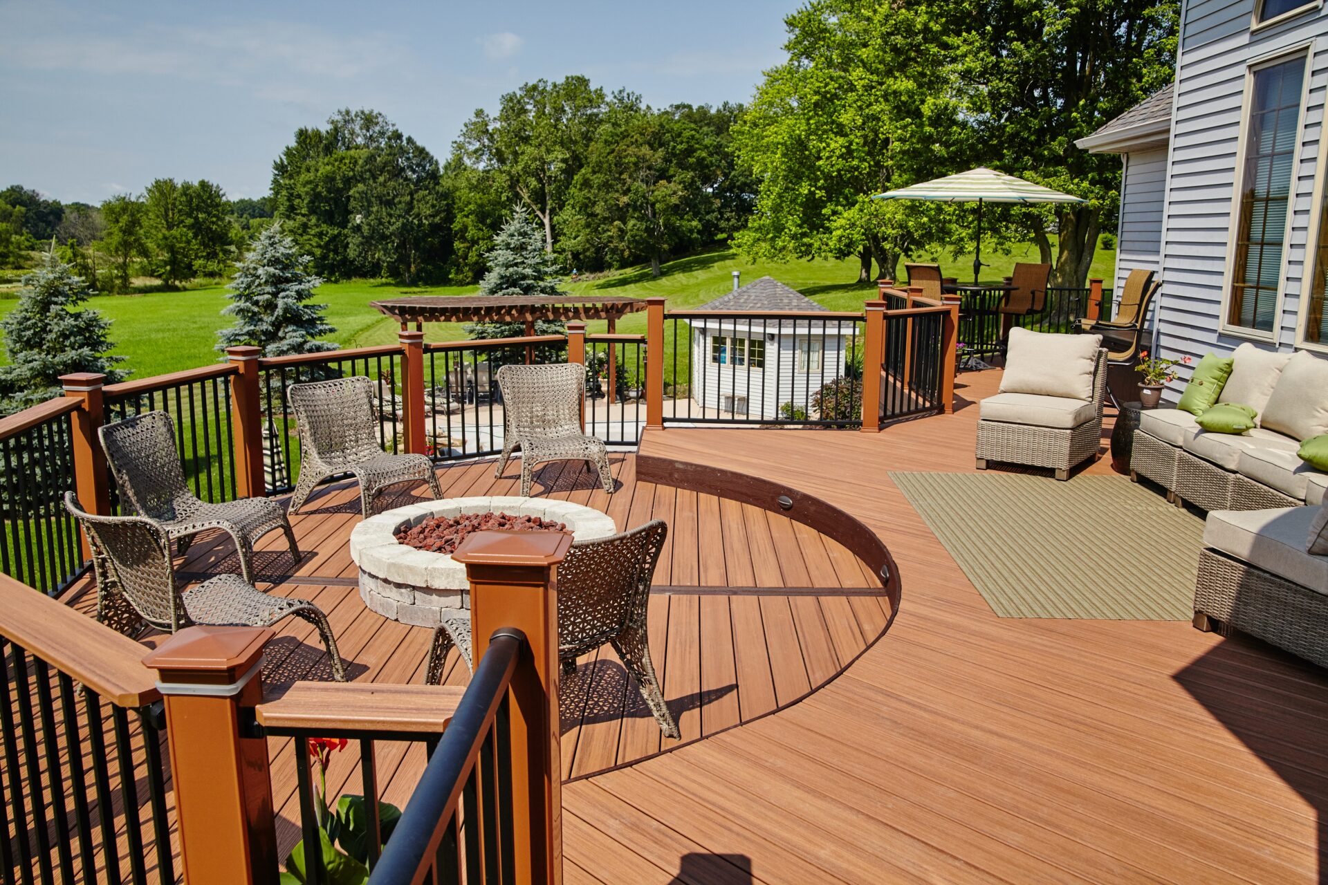 Spacious backyard deck with wicker seating around a built-in fire pit, outdoor sofa, and scenic lawn views